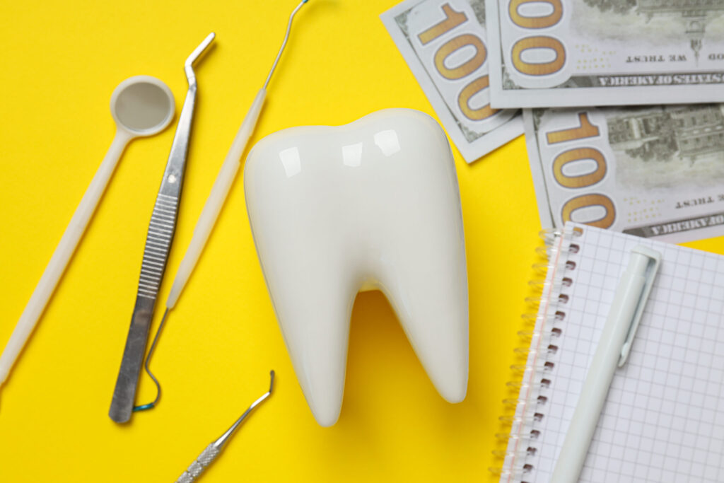 Dental tools, money, decorative tooth and notepad on yellow back