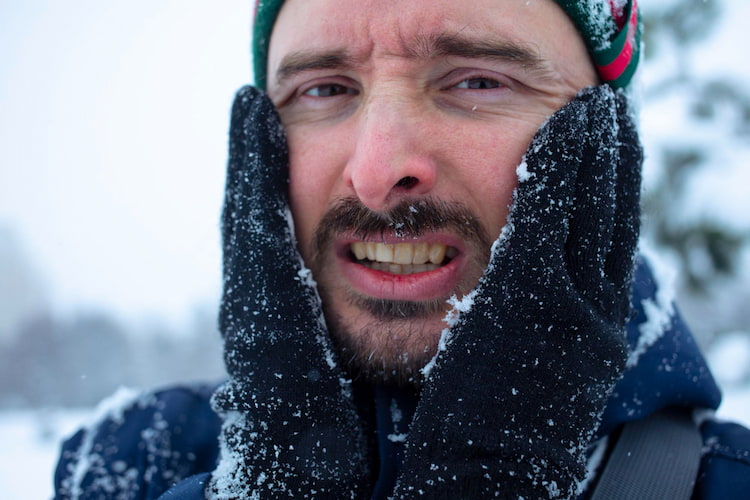 a man in a snowy weather is holding his cheeks with hands, irritated by his sensitive teeth in cold weather.