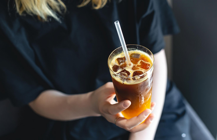 a person is holding a glass of iced coffee with a straw in it.