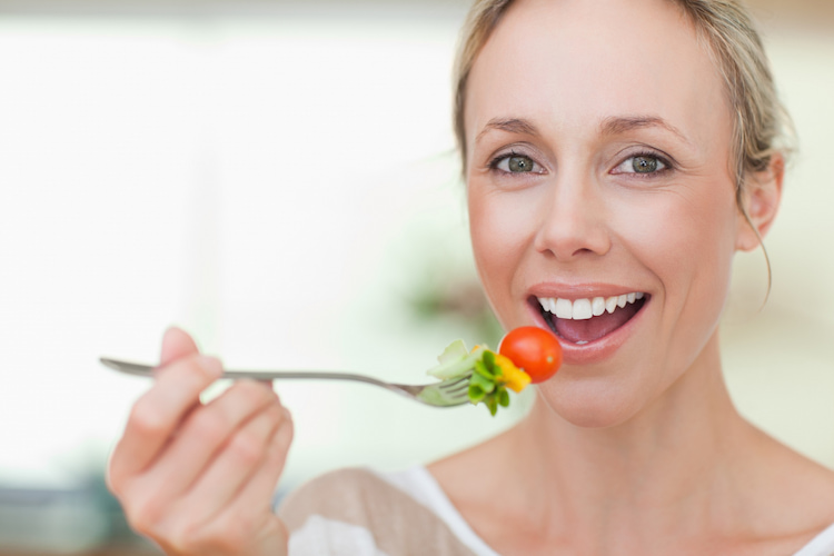 a smiling vegan woman putting food in her mouth with a fork. 