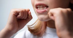 a child is holding a dental floss between her teeth.