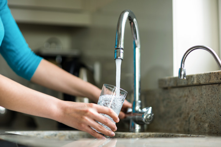 a person is filling a glass with tap water in the kitchen. 
