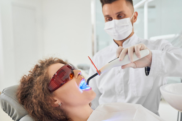 Woman lying in a dental chair undergoing a teeth whitening procedure.