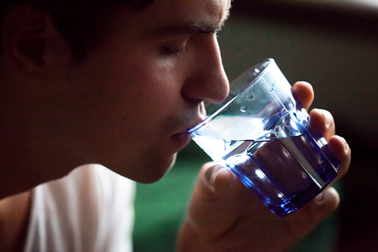 Close-up of a young man drinking water at a rave to stay hydrated and prevent dry mouth