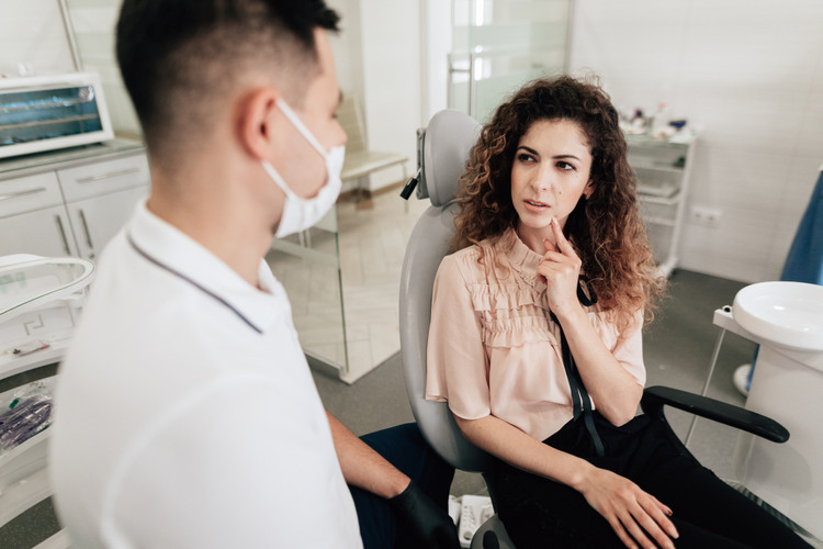 Young woman sitting in a dental clinic talking with a dentist about MDMA teeth damage while seated in a dental chair