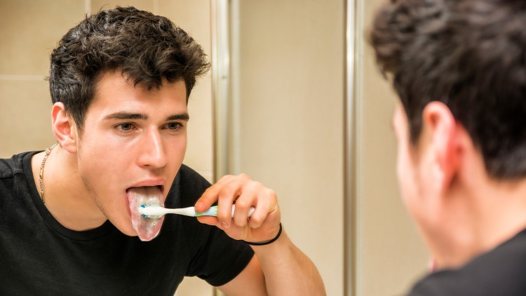 Young man brushing his tongue in front of a mirror to get rid of bad breath after eating shawarma