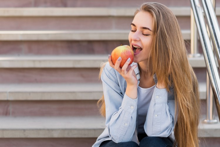 Young woman sitting on stairs biting an apple to relieve bad breath after eating shawarma