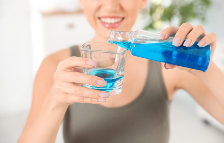 Young woman pouring blue mouthwash into a glass for oral hygiene before bedtime