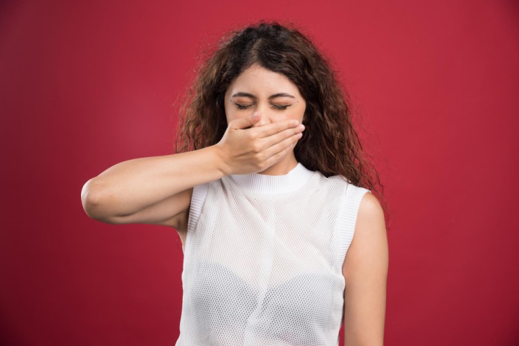 Young woman covering her mouth due to bad breath with eyes closed
