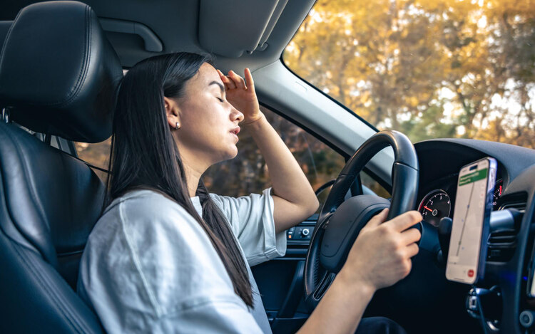 Woman driver experiencing headache in traffic jam, eyes closed and hand on forehead