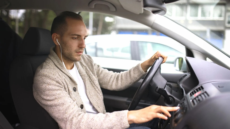A male driver wearing earbuds and listening to music to manage stress and help prevent stress-related teeth grinding (bruxism) in Toronto traffic
