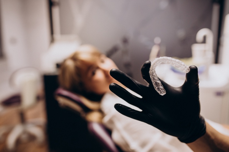 Dentist holding a night guard in hands in a dental clinic with a patient laying on a dental chair in the background