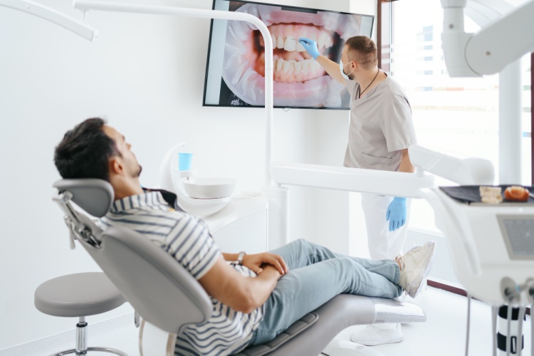 Male patient sitting on a dental chair for a dental check-up while the dentist reviews his dental X-rays in a clinic setting