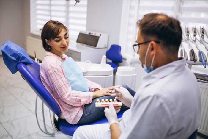 A male dentist consulting with a female patient in a modern dental clinic, explaining the differences between dental implants vs veneers using dental models.