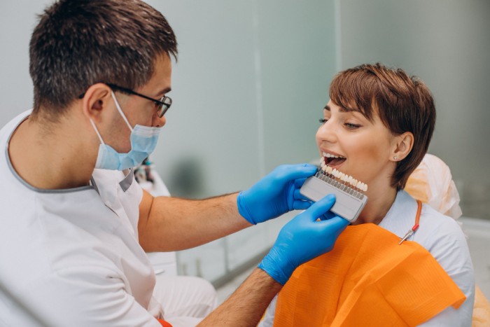 A male dentist comparing a set of porcelain veneers with a female patient's teeth to select the best shape and shade match for her.