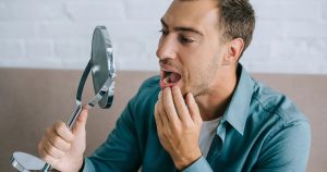 A man carefully examining his teeth in the mirror, slightly concerned about the presence of black spots on teeth