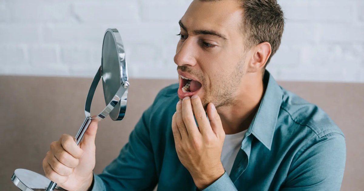 A man carefully examining his teeth in the mirror, slightly concerned about the presence of black spots on teeth
