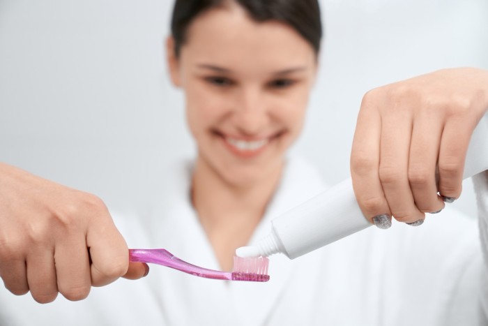 A young woman applying toothpaste to her toothbrush to help prevent black spots on teeth
