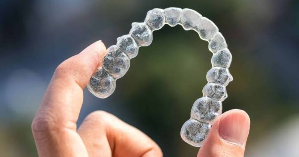 Close-up of an Invisalign aligner being held up in the air in front of the camera, with the aligner looking slightly cloudy.