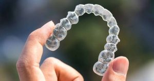 Close-up of an Invisalign aligner being held up in the air in front of the camera, with the aligner looking slightly cloudy.