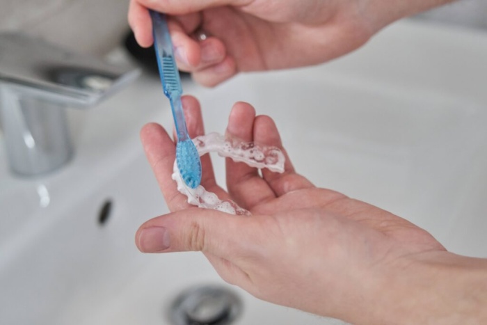 Cleaning an Invisalign aligner with a toothbrush to demonstrate how to clean Invisalign.