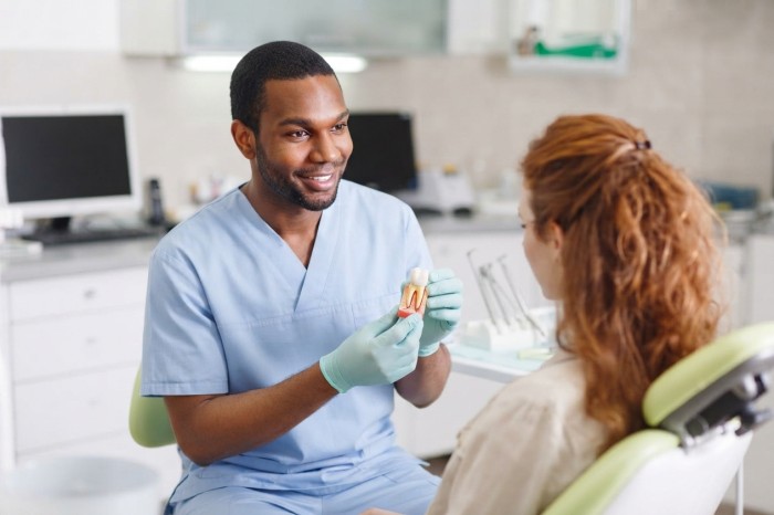 Dentist explaining different types of dental crowns to a patient while holding a crown model