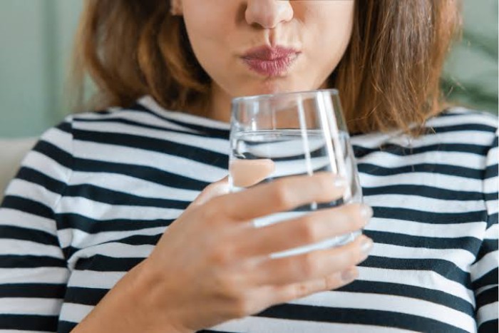 A young woman holding a glass and rinsing her mouth with salt water