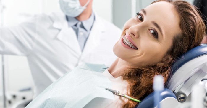 A young woman with braces sitting in a dental chair for a routine checkup, smiling at the camera.