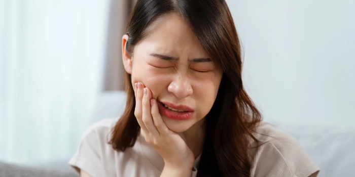 A woman who delayed treatment for a dead tooth and is now experiencing severe pain, holding her jaw with her hand.