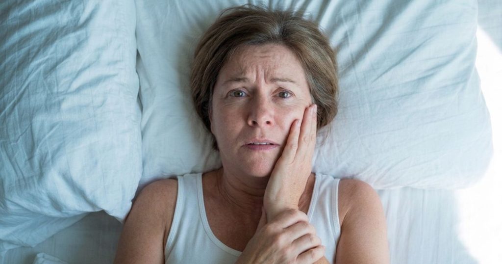 A worried middle-aged woman lying in bed, holding her jaw after her tooth filling fell out
