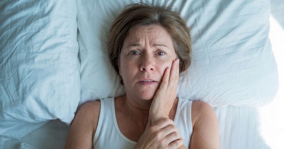 A worried middle-aged woman lying in bed, holding her jaw after her tooth filling fell out