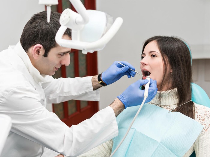 A male dentist examining a gum boil on a female patient.